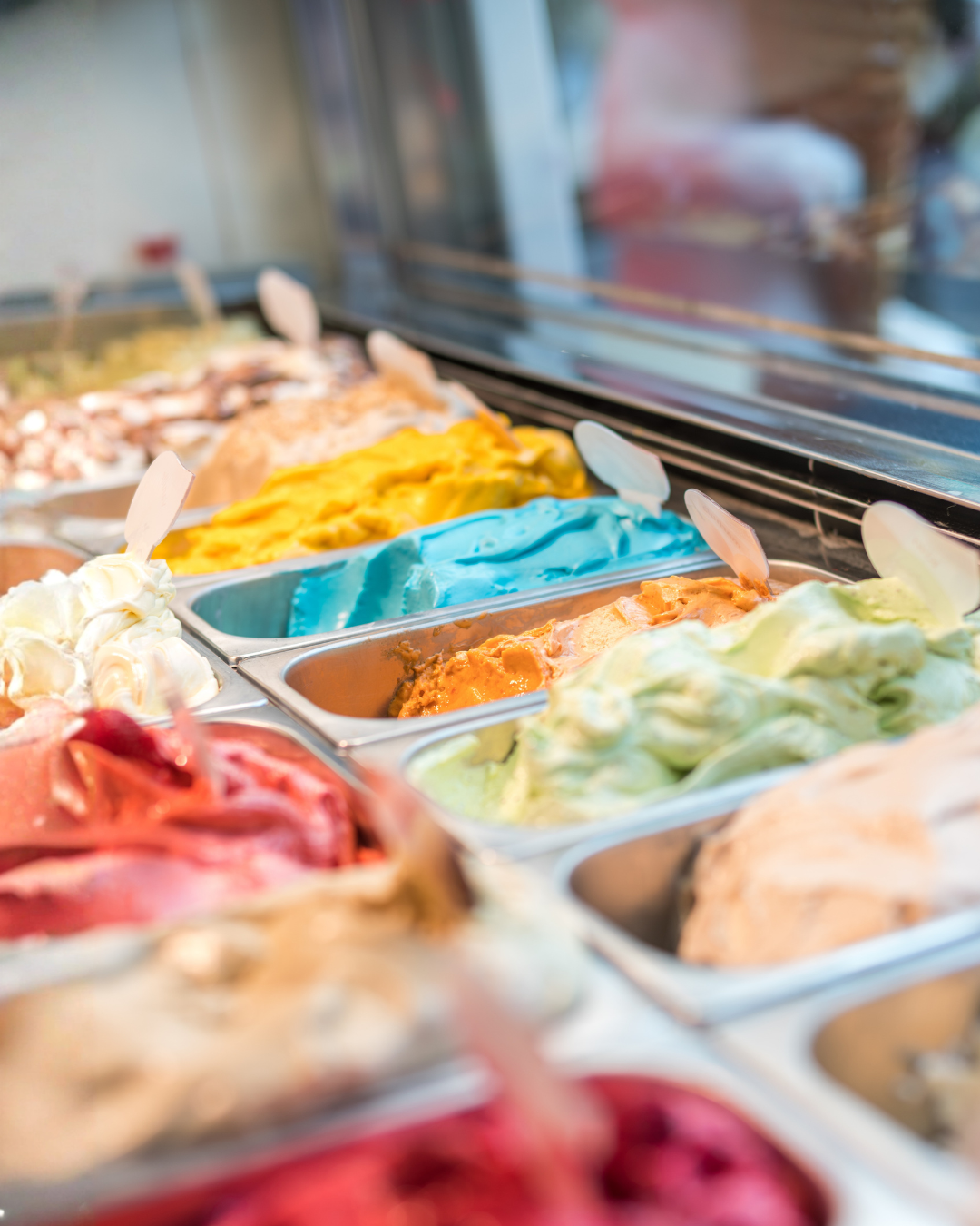 Close-up of various vibrant gelato flavors in a display case, featuring bright blue, orange, and green scoops.