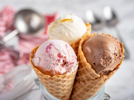 three classic waffle cones held together, each topped with a scoop of ice cream. One has vanilla, one has strawberry, and one has chocolate ice cream.